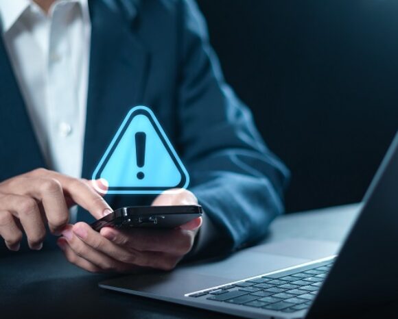 Maintenance concept. Businessman using smartphone with triangle caution warning sign for notification error. System failure and security issues.