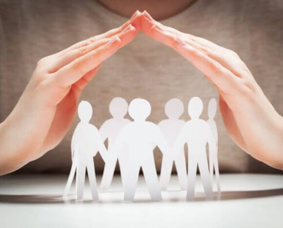 Papiermenschen unter Händen in Geste des Schutzes.. Konzept der Versicherung