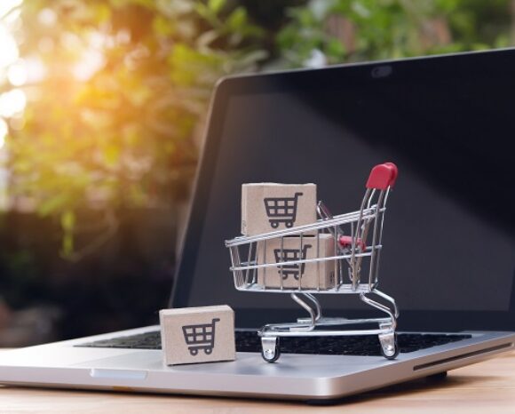 Online einkaufen. Karton mit Einkaufswagen-Logo in einem Einkaufswagen auf der Laptop-Tastatur.