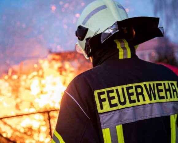 Mensch in Feuerwehruniform steht vor Feuer