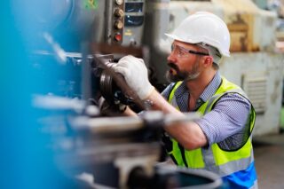 Arbeiter mit Schutzbrille steuert Drehmaschine, um Komponenten zu bohren. Konzept von Maschinensicherheit