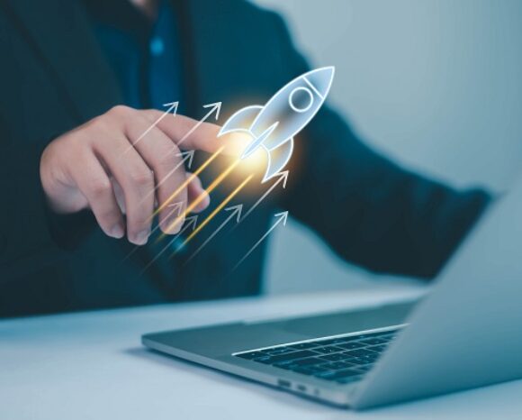 Geschäftsperson tippt auf ein digitales Raketen-Symbol, das über einem Laptop aufsteigt – Symbol für Start-up-Wachstum und Innovation.