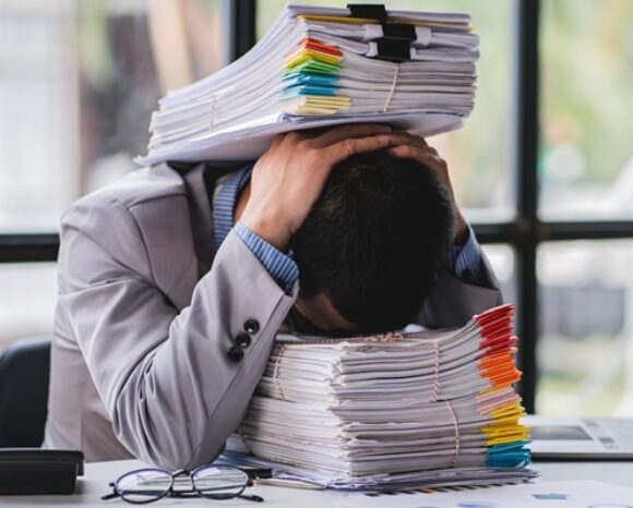 Mann mit Händen auf dem Kopf und Kopf auf Dokumentenstapel