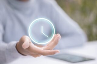 Eine Frauenhand hält ein virtuelles, leuchtendes Uhrsymbol auf ihrer Handfläche.