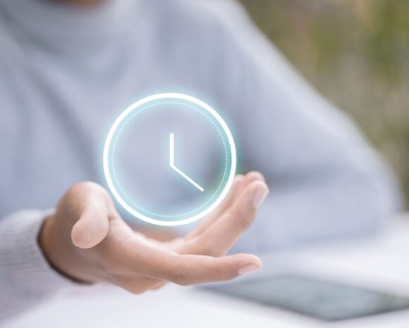Eine Frauenhand hält ein virtuelles, leuchtendes Uhrsymbol auf ihrer Handfläche.